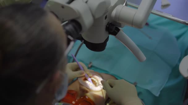 Vrouwelijke tandarts behandelt een vrouw. Ze gebruikt een microscoop om de tand nauwkeuriger en zelfverzekerder te onderzoeken. — Stockvideo