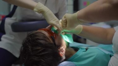 Beyaz üniformalı ve beyaz eldivenli kadın dişçi bir erkeği tedavi eder.