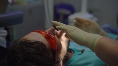 Beyaz üniformalı ve beyaz eldivenli kadın dişçi bir erkeği tedavi eder.