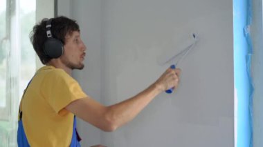 Profesyonel bir inşaat işçisi paten boyacısı kullanarak duvarı boyuyor. Kulaklıklarıyla müzik dinliyor. Slowmotion shot.