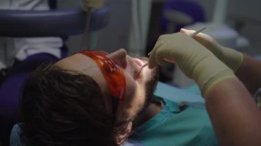 Beyaz üniformalı ve beyaz eldivenli kadın dişçi bir erkeği tedavi eder.