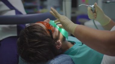 Beyaz üniformalı ve beyaz eldivenli kadın dişçi bir erkeği tedavi eder.