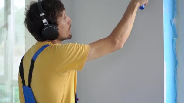 Um homem trabalhador da construção profissional pintar a parede usando um pintor de rolos. Ele ouve música nos auscultadores. Slowmotion shot. — Vídeo de Stock