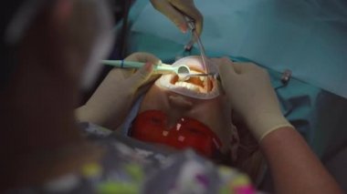 Kadın dişçi bir kadını tedavi eder. Dişi, mikroskop kullanarak daha dikkatli ve emin bir şekilde inceler.