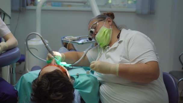 Mulher dentista em um uniforme branco e luvas brancas trata um homem — Vídeo de Stock