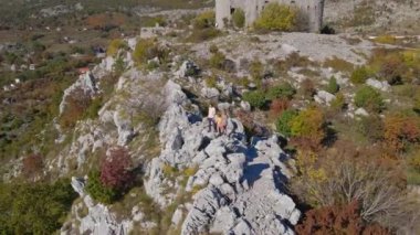 Hava görüntüsü. Turist ailesi, baba ve oğul Karadağ 'daki Kosmach Kalesini ziyaret etti. Uzaktan Budva şehrini izleyen bir tepede dikilirken insansız hava aracı onların etrafında dönüyor.