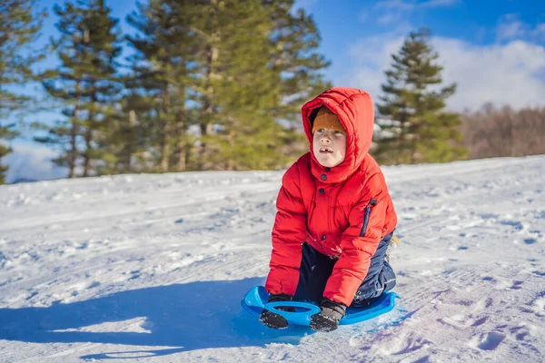 Счастливый и позитивный маленький мальчик, наслаждающийся катанием на санках и холодной погодой на открытом воздухе, концепция зимних развлечений — стоковое фото