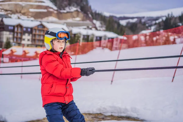 El chico usa un elevador de entrenamiento. Esquí infantil en las montañas. Niño activo con casco de seguridad, gafas y bastones. Carrera de esquí para niños pequeños. Deportes de invierno para la familia. Clases de esquí para niños en la escuela alpina — Foto de Stock