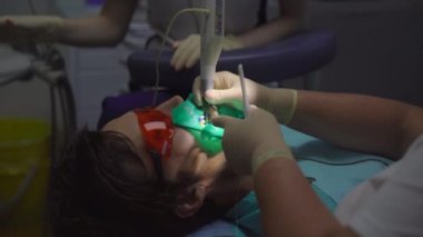 Kadın dişçi bir erkeği tedavi eder. Bir dişin sinirlerini sökme süreci.