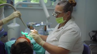 Beyaz üniformalı ve beyaz eldivenli kadın dişçi bir erkeği tedavi eder.