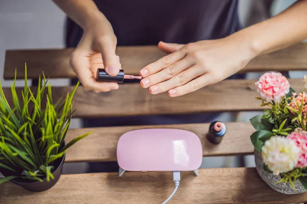 Mulher jovem faz manicure com gel polonês e lâmpada UV em tons rosa — Fotografia de Stock