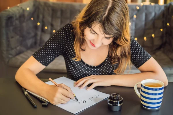 Calígrafa Joven escribe frase en papel blanco. Inscribiendo letras ornamentales decoradas. Caligrafía, diseño gráfico, letras, escritura a mano, concepto de creación —  Fotos de Stock