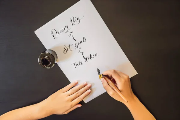 Dream big set goals take action. Calligrapher Young Woman writes phrase on white paper. Inscribing ornamental decorated letters. Calligraphy, graphic design, lettering, handwriting, creation concept — Stock Photo, Image