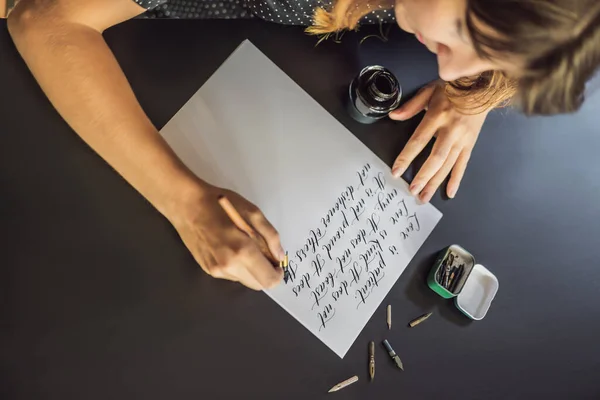 Calígrafo manos escribe frase en papel blanco. Frase bíblica sobre el amor Inscripción de letras ornamentales decoradas. Caligrafía, diseño gráfico, letras, escritura a mano, concepto de creación —  Fotos de Stock