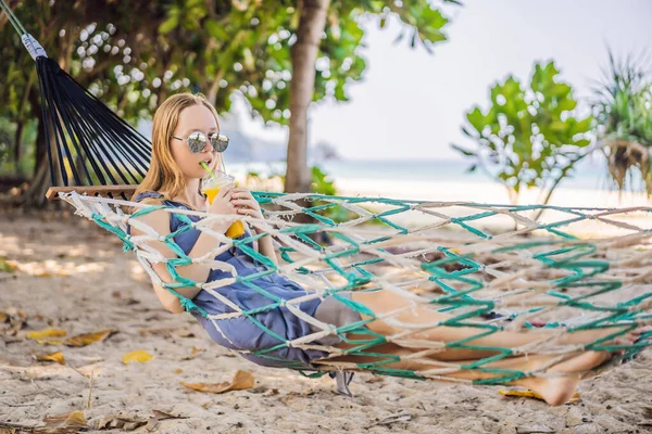 Mladá žena na pláži v houpací síti s nápojem — Stock fotografie