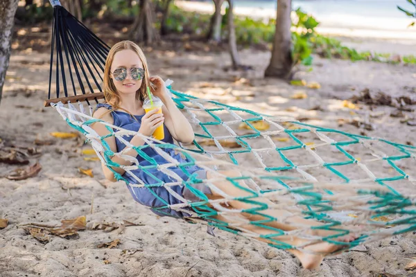 Jovem mulher na praia em uma rede com uma bebida — Fotografia de Stock