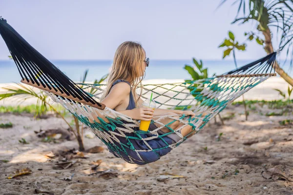 Giovane donna sulla spiaggia su un'amaca con un drink — Foto Stock