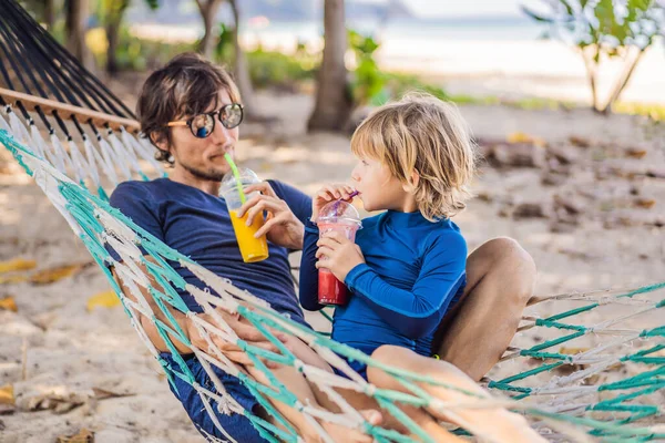 Papá y su hijo se divierten en una hamaca con una bebida — Foto de Stock