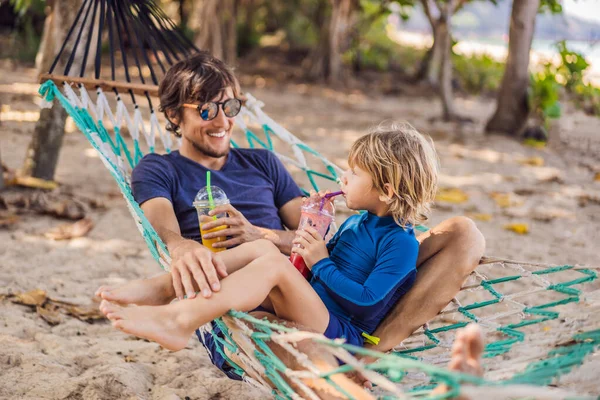 Papá y su hijo se divierten en una hamaca con una bebida — Foto de Stock