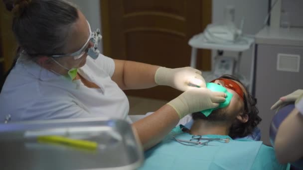 Žena zubař v bílé uniformě a bílé rukavice zachází s mužem — Stock video