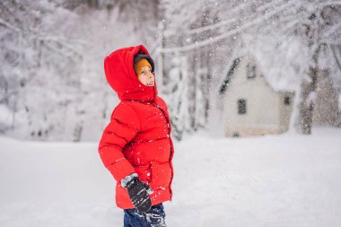 Mavi kışlık elbiseli komik küçük çocuk kar yağışı sırasında yürür. Çocuklar için açık hava kış aktiviteleri. Sevimli bir çocuk, kalın bir şapka takıyor gözlerinin üstüne, diliyle kar taneleri yakalıyor.