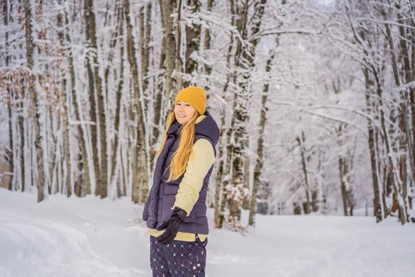 Šťastná hezká kavkazská mladá žena v teplých šatech a klobouku, stojící v modrém zasněženém lese a dívající se stranou. Usmívající se roztomilá dívka těší slunečný den v zimě, venku — Stock fotografie