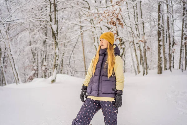 Joyeux jolie jeune femme caucasienne en vêtements chauds et chapeau debout dans la forêt enneigée bleue et regardant loin. Souriant fille mignonne profitant d'une journée ensoleillée en hiver, en plein air — Photo
