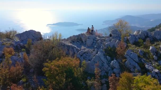 Flygskott. Familj till turisterna far mor och son besöker fästningen Kosmach i Montenegro. Drone flyger över dem när de står på en kulle och observerar staden Budva i fjärran — Stockvideo