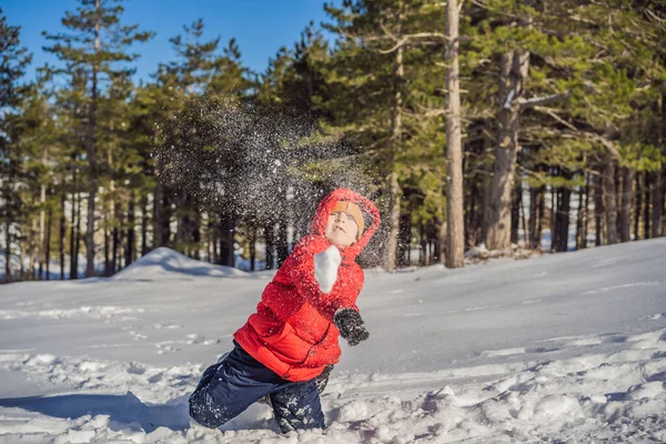 青い冬の服を着た面白い男の子が雪の中を歩く。子供のための屋外冬の活動。かわいい子供を身に着けている暖かい帽子低い彼の目の上に雪の結晶をキャッチ彼の舌 — ストック写真