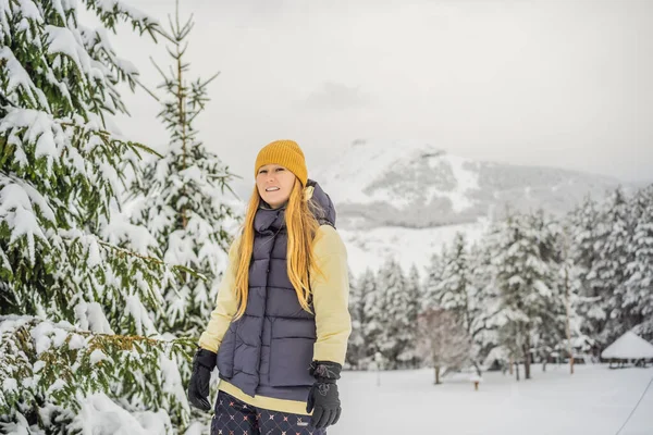 Joyeux jolie jeune femme caucasienne en vêtements chauds et chapeau debout dans la forêt enneigée bleue et regardant loin. Souriant fille mignonne profitant d'une journée ensoleillée en hiver, en plein air — Photo