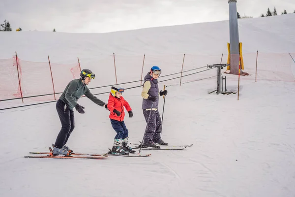 Mom and son are learning to ski with an instructor. Active toddler kid with safety helmet, goggles and poles. Ski race for young children. Winter sport for family. Kids ski lesson in alpine school — Stock Photo, Image