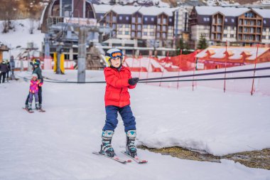 Çocuk eğitim asansörü kullanıyor. Çocuk dağlarda kayak yapıyor. Güvenlik kaskı, gözlüğü ve direkleri olan aktif bir çocuk. Küçük çocuklar için kayak yarışı. Aile için kış sporu. Alp okulunda çocuklar kayak dersi alıyor.