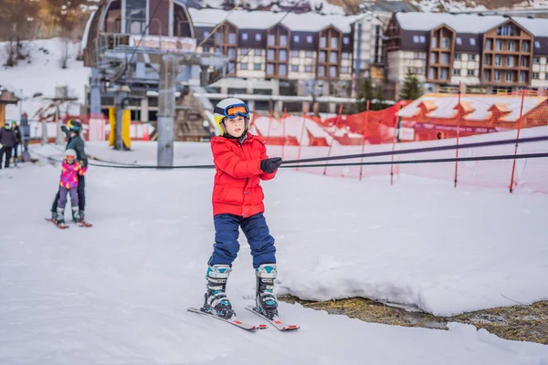 Le garçon utilise un ascenseur d'entraînement. Ski d'enfant en montagne. Enfant tout-petit actif avec casque de sécurité, lunettes et bâtons. Course de ski pour jeunes enfants. Sport d'hiver pour la famille. Cours de ski pour enfants à l'école alpine — Photo