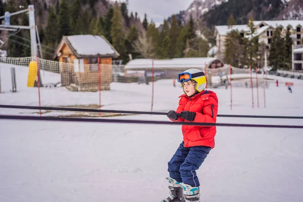 De jongen gebruikt een trainingslift. Kinderskiën in de bergen. Actief peuter kind met veiligheidshelm, bril en stokken. Ski race voor jonge kinderen. Wintersport voor familie. Skilessen voor kinderen op de alpine school — Stockfoto