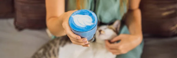 Young woman having a mediterranean breakfast seated at sofa and with her cat and drinks Trendy drink: Blue latte. Hot butterfly pea latte or blue spirulina latte BANNER, LONG FORMAT — Stock Photo, Image