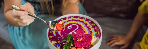 BANNER, LONG FORMAT Mother and son having a medanean breakfast seated at the sofa and eats Healthy tropical breakfast, smoothie bowl with tropical fruits, decorated with a pattern of colorful — стоковое фото