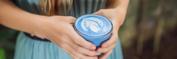 Egy mediterrán reggelivel rendelkező fiatal nő a kanapén ülve iszik Trendy drink: Blue latte. Forró pillangó borsó latte vagy kék spirulina latte Banner, Hosszú formátum — Stock Fotó