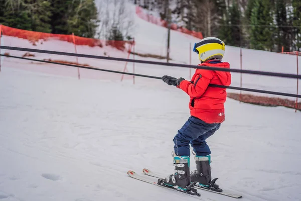 Junge benutzt einen Trainingslift. Kinderskifahren in den Bergen. Aktives Kleinkind mit Schutzhelm, Schutzbrille und Stöcken. Skirennen für kleine Kinder. Wintersport für die Familie. Kinder-Skikurs in der Alpinschule — Stockfoto