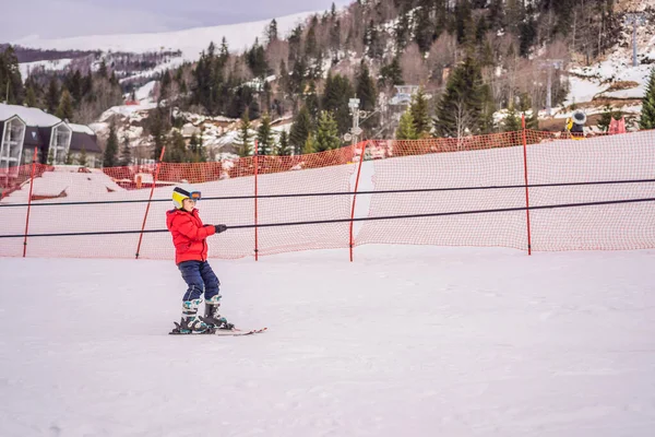 De jongen gebruikt een trainingslift. Kinderskiën in de bergen. Actief peuter kind met veiligheidshelm, bril en stokken. Ski race voor jonge kinderen. Wintersport voor familie. Skilessen voor kinderen op de alpine school — Stockfoto