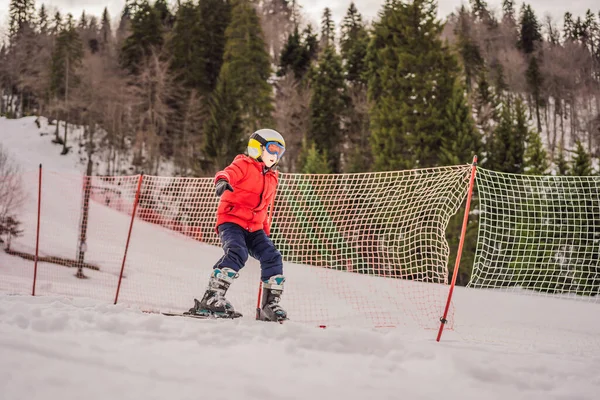 Dětské lyžování v horách. Aktivní batole s bezpečnostní helmou, brýlemi a tyčemi. Lyžařský závod pro malé děti. Zimní sport pro rodinu. Dětská lekce lyžování v alpské škole. Malé závodní lyžování ve sněhu — Stock fotografie