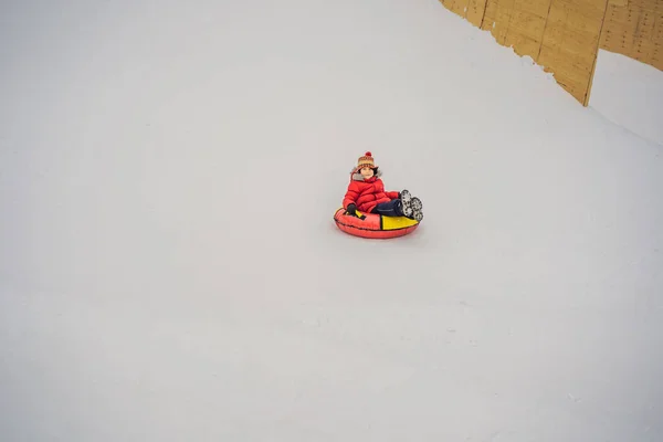 Criança se divertindo no tubo de neve. O rapaz está a montar um tubo. Diversão de inverno para crianças — Fotografia de Stock
