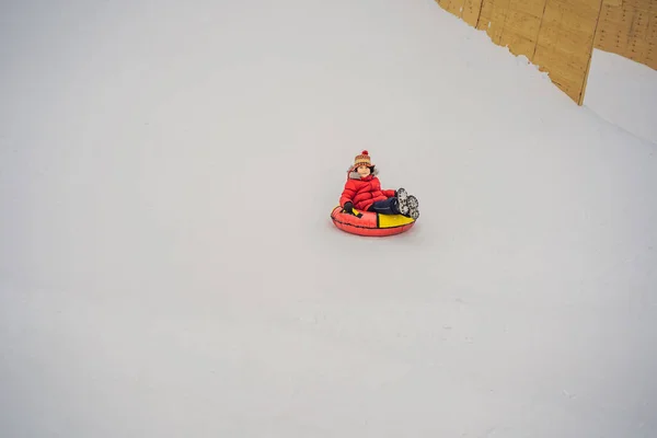 Niño divirtiéndose en tubo de nieve. El chico está montando un tubo. Diversión de invierno para niños —  Fotos de Stock