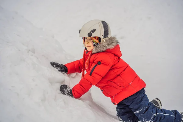 Милый мальчик взбирается на снежную гору — стоковое фото