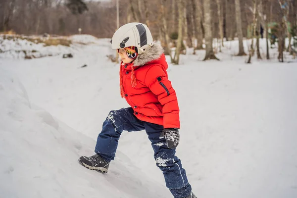Милый мальчик взбирается на снежную гору — стоковое фото
