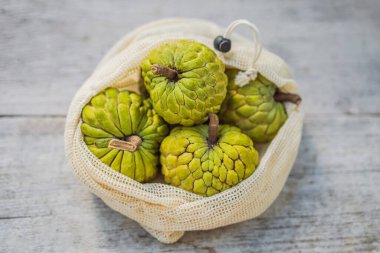 Cherimoya in a reusable bag on a stylish wooden kitchen surface. Zero waste concept, plastic free concept. Healthy clean eating diet and detox. Summer fruits