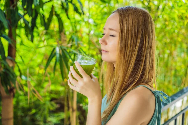 Giovane donna beve succo di sedano, bevanda sana, mazzo di sedano su uno sfondo di legno — Foto Stock