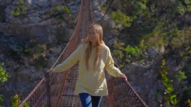 Karadağ 'daki Moraca nehri kanyonu üzerinde eski bir metal ip köprü. Sarı ceketli bir kadın köprü boyunca yürüyor.