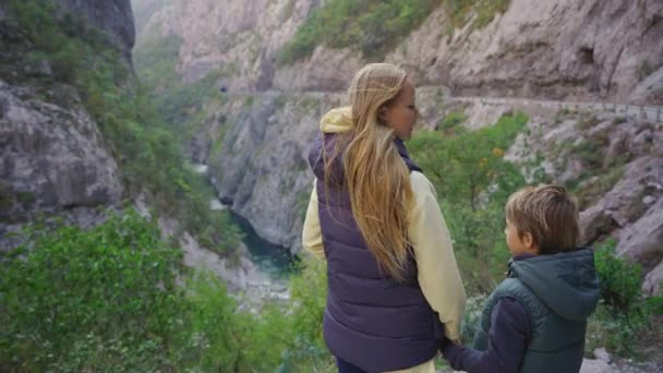 Kobieta i jej syn stoją przy drodze, obserwując wspaniały kanion rzeki Morachy. Podróż do Czarnogóry koncepcja — Wideo stockowe