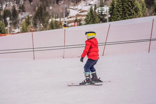 Παιδικό σκι στα βουνά. Ενεργό παιδί νηπίων με κράνος ασφαλείας, γυαλιά και κοντάρια. Αγώνας σκι για μικρά παιδιά. Χειμερινό άθλημα για την οικογένεια. Μαθήματα σκι για παιδιά σε αλπική σχολή. Μικρή σκιέρ αγωνιστικά στο χιόνι — Φωτογραφία Αρχείου