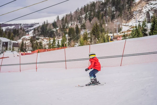 Ski d'enfant en montagne. Enfant tout-petit actif avec casque de sécurité, lunettes et bâtons. Course de ski pour jeunes enfants. Sport d'hiver pour la famille. Cours de ski pour enfants à l'école de ski alpin. Petit skieur de course dans la neige — Photo